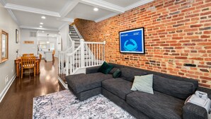 A modern living room with a brick wall, a sectional sofa, and a staircase leading to an upper level.