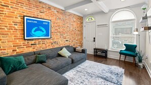 A living room with a brick wall, a gray sectional sofa, a blue rug, and a teal chair.