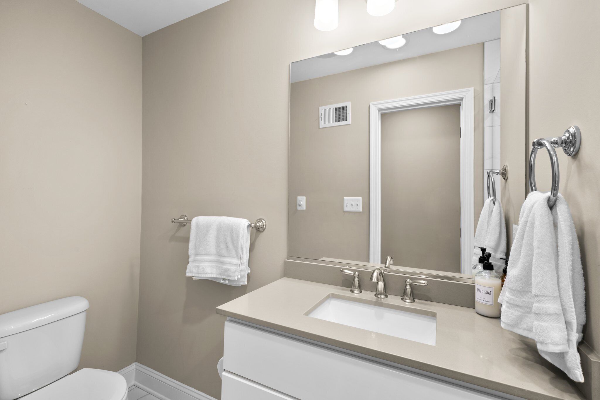 A bathroom with a beige wall, a white sink, a mirror, and a towel rack.