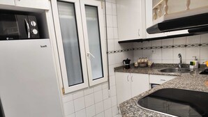A kitchen with white cabinets, a black stove, a double sink, and a microwave. - Casa Genoveva . 2ª Linea DE Playa SAN Lorenzo-gijon (Gijón)