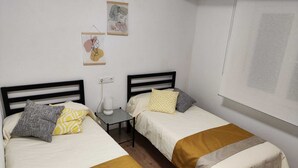 A simple, clean room with two beds, a small table, and a wall-mounted lamp. - Casa Genoveva . 2ª Linea DE Playa SAN Lorenzo-gijon (Gijón)