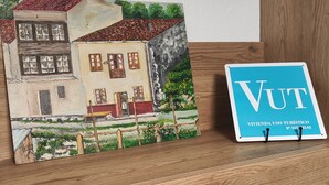 A framed painting of a two-story building with a red roof and a small porch, and a sign with the text "VUT" and "VIVIENDA USO TURISTICO" on a wooden shelf. - Casa Genoveva . 2ª Linea DE Playa SAN Lorenzo-gijon (Gijón)