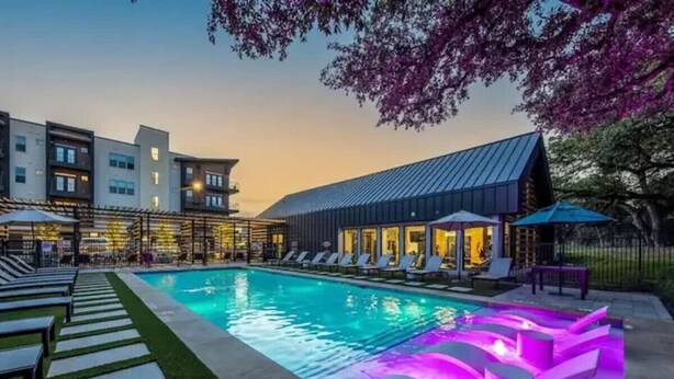 A swimming pool with a water feature, lounge chairs, and a building with a modern design in the background. - Luxurious New Unit|2Bd2Ba|Pool, Golf Sim (Austin)