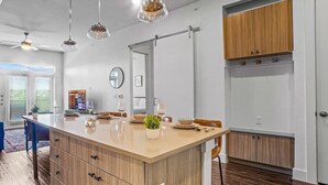 A modern kitchen with a central island, wooden cabinets, pendant lighting, and a view to the outside. - Luxurious New Unit|2Bd2Ba|Pool, Golf Sim (Austin)