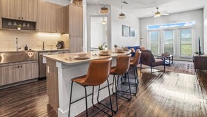 Een moderne keuken met houten kastjes, een centraal eiland met barstoelen en een eethoek met een bank en salontafel.