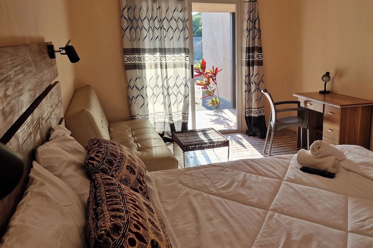 A hotel room with a bed, a desk, and a chair. There is a window with curtains and a view of the outside.