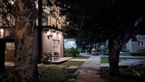 Un espacio exterior nocturno con un sendero que lleva a un edificio, rodeado de árboles y plantas.