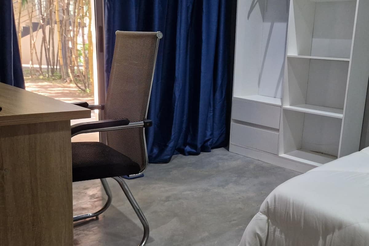 A hotel room with a bed, a desk, a chair, a window with curtains, and a built-in shelf unit.