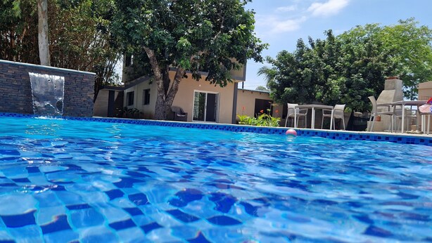 Una piscina con mosaicos azules, rodeada de árboles y un edificio con una cascada.