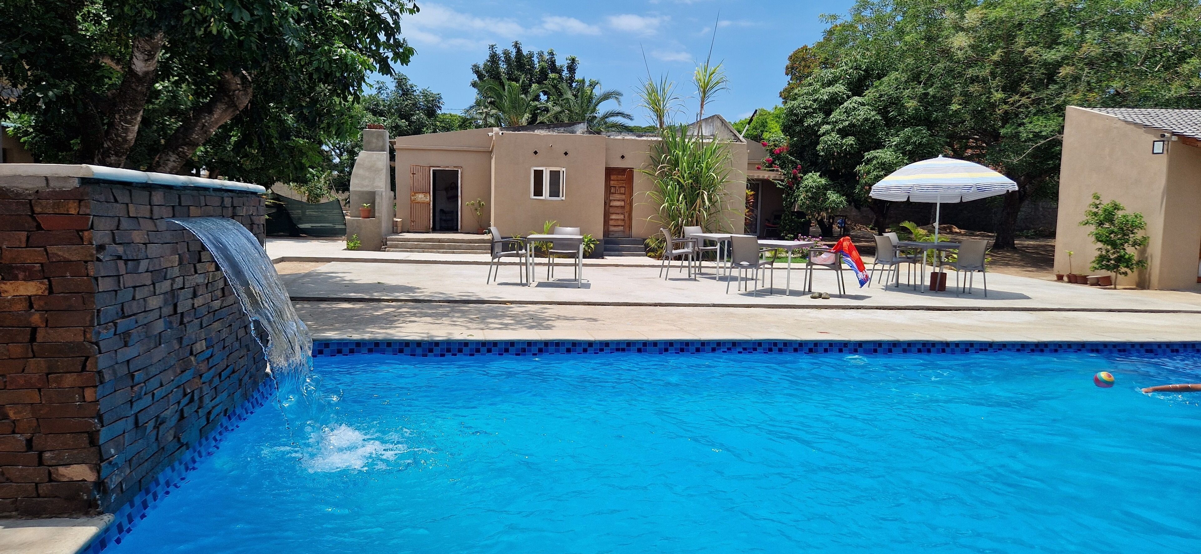 Una piscina con cascada de ladrillo, asientos al aire libre y un pequeño edificio con puerta y ventanas.