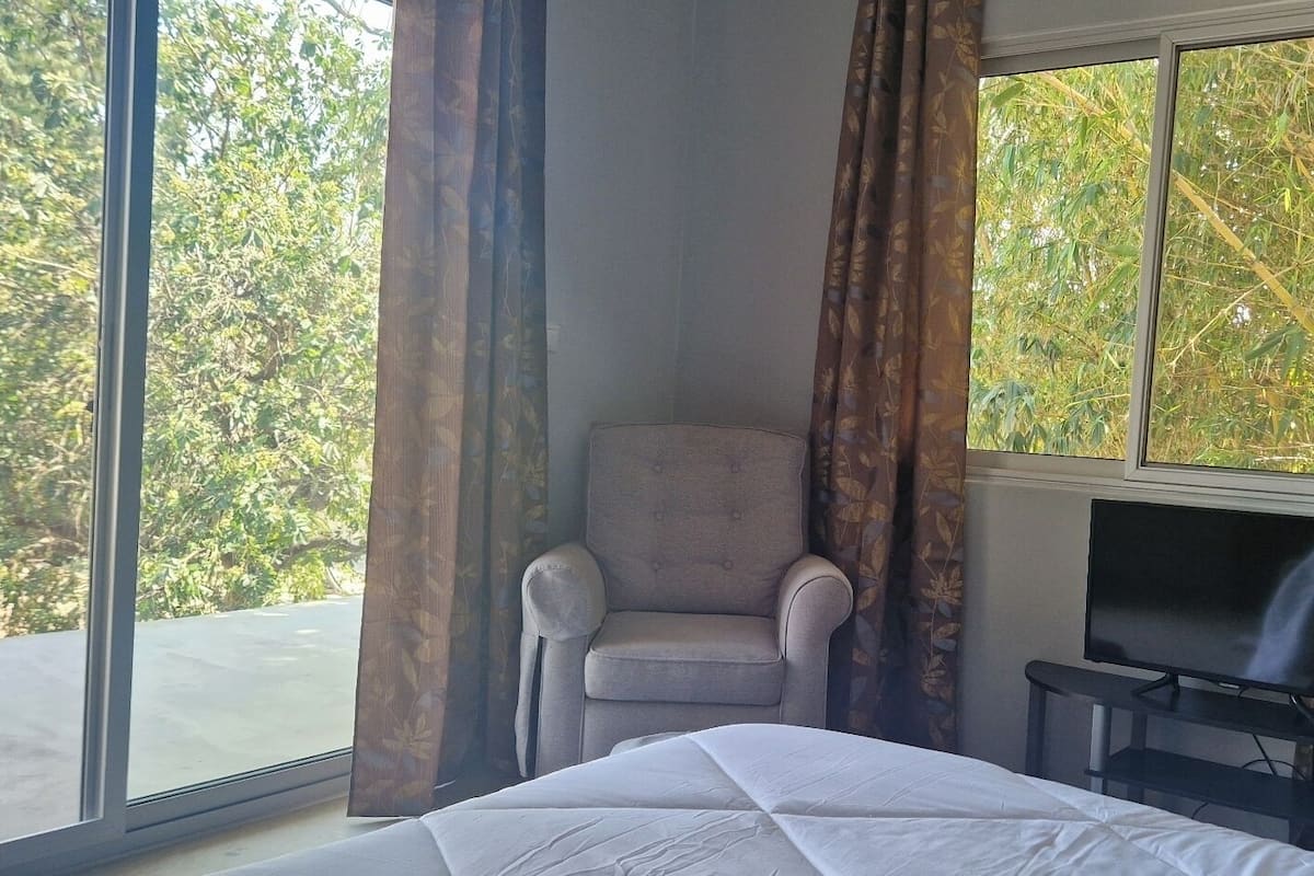 A hotel room with a bed, a TV, a chair, and a large window with curtains.