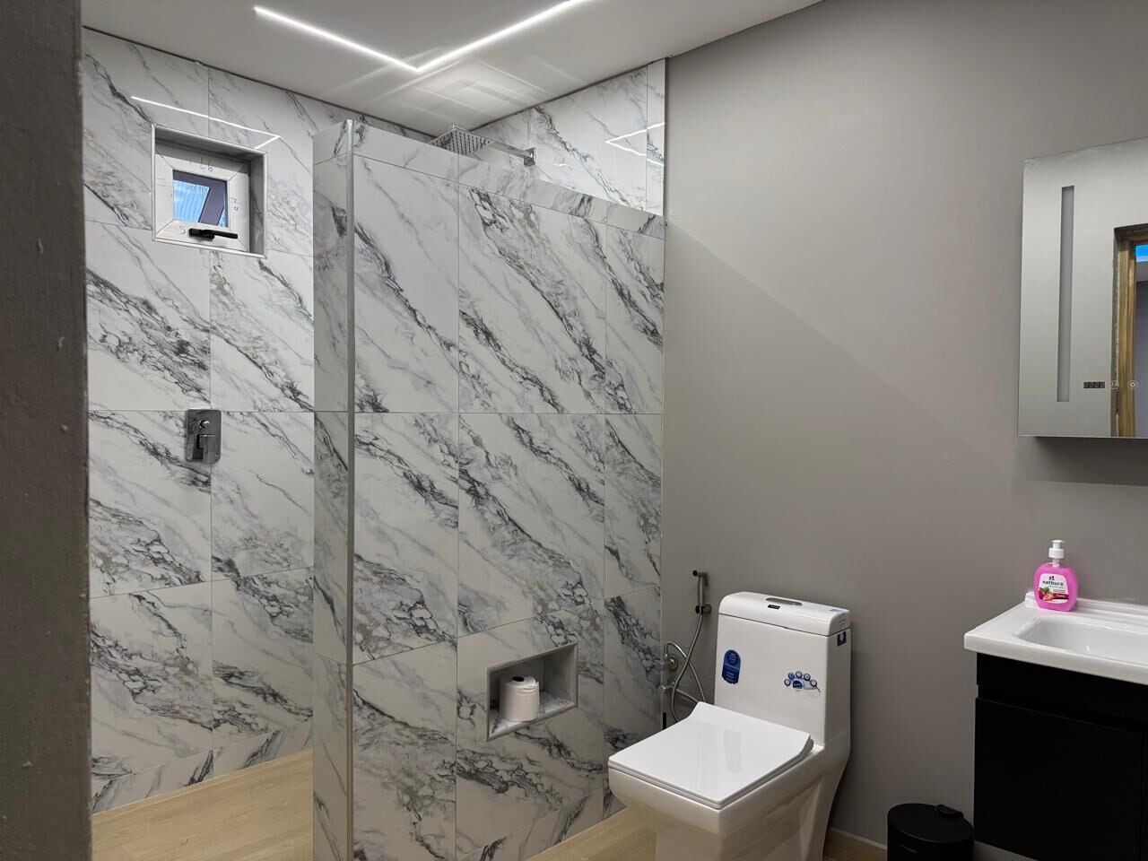 A bathroom with a marble wall, a toilet, a sink, and a shower area.
