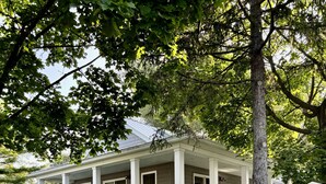 A covered porch with wicker furniture, a white fence, and a tree in the foreground.