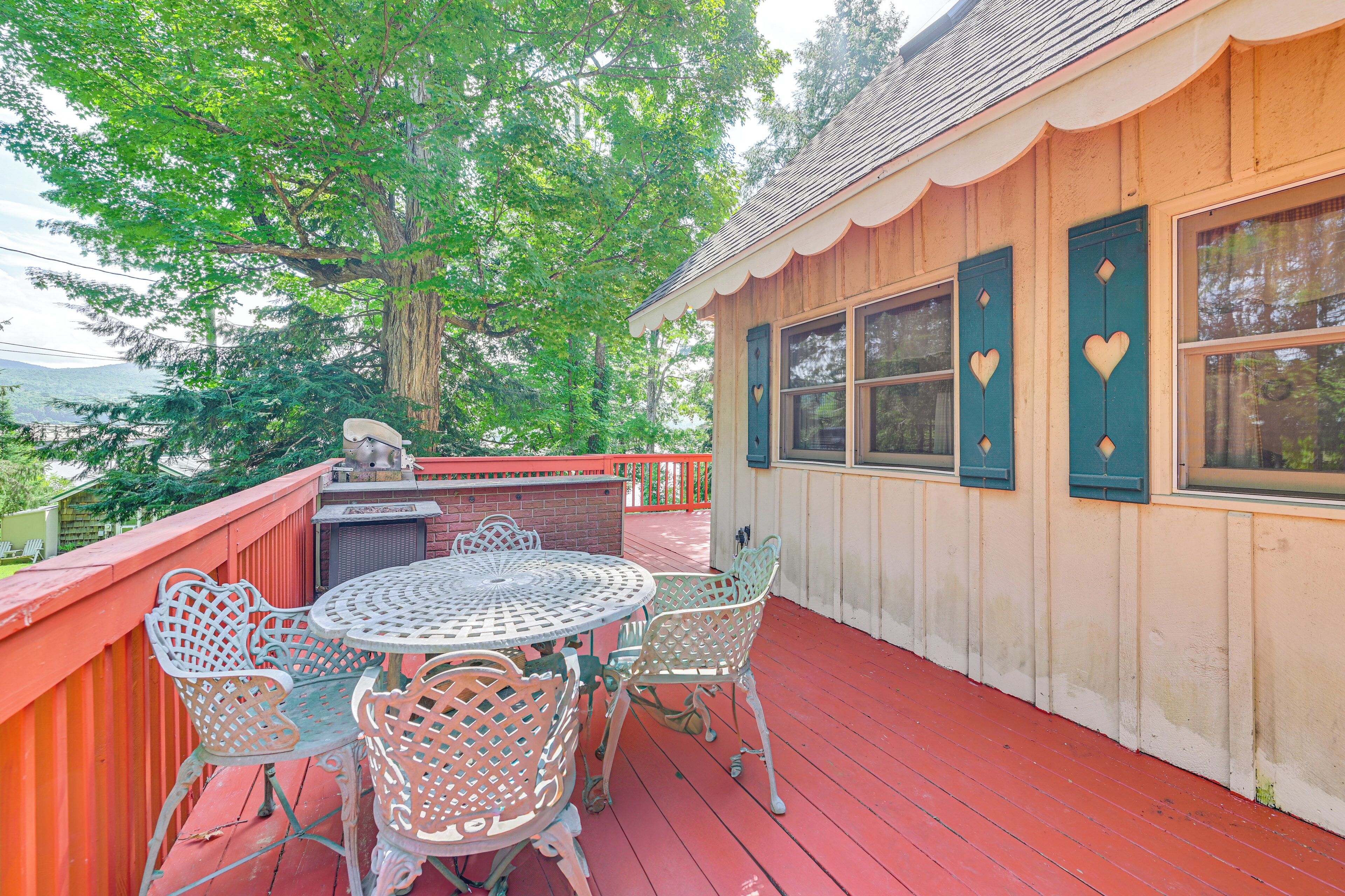 A wooden deck with a red railing, a round metal table with chairs, and a large tree in the background.