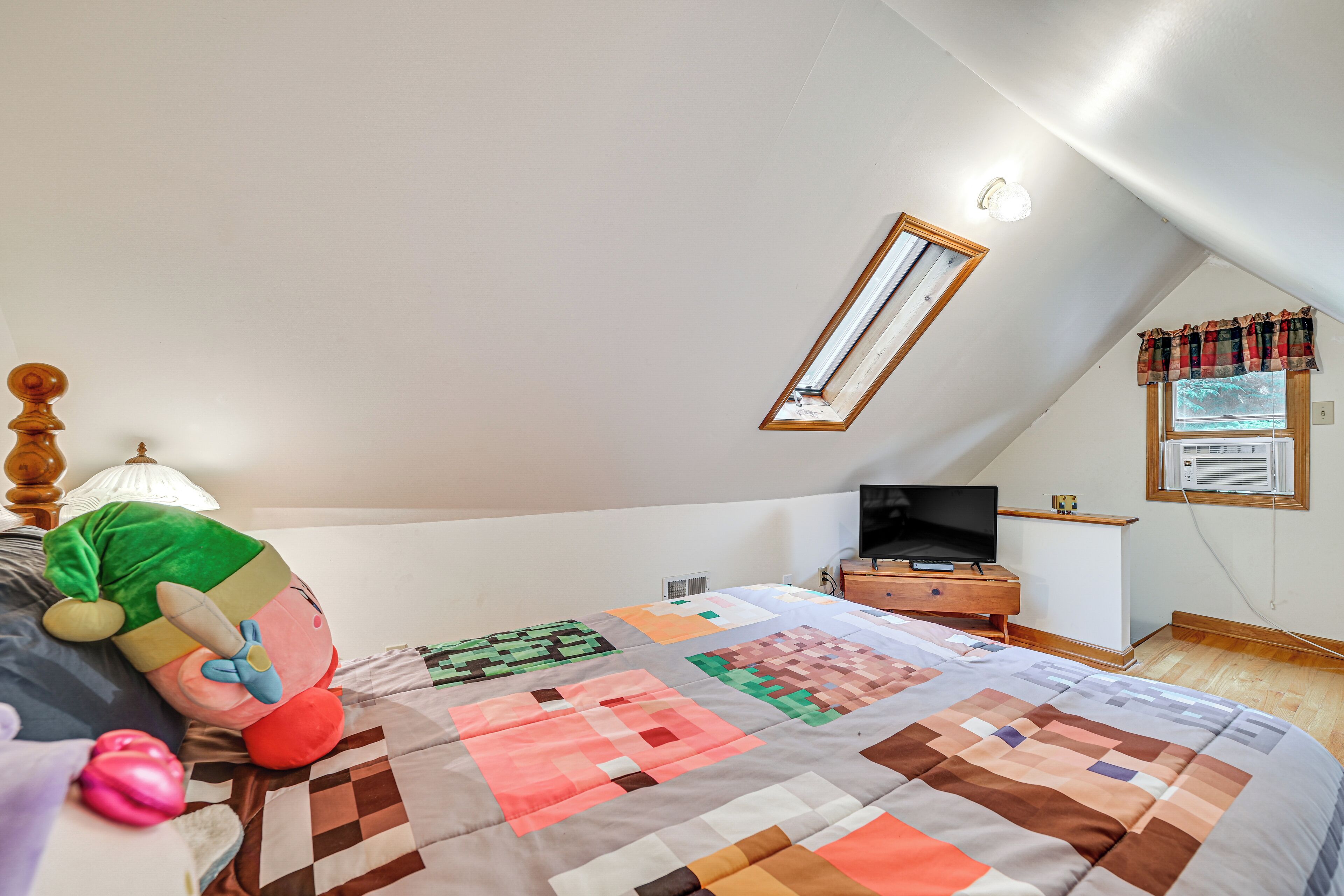 A bedroom with a large bed, a television on a wooden nightstand, a window with a view, and a ceiling light.