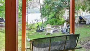 A porch with a swing, two Adirondack chairs, and a covered area with a tent.