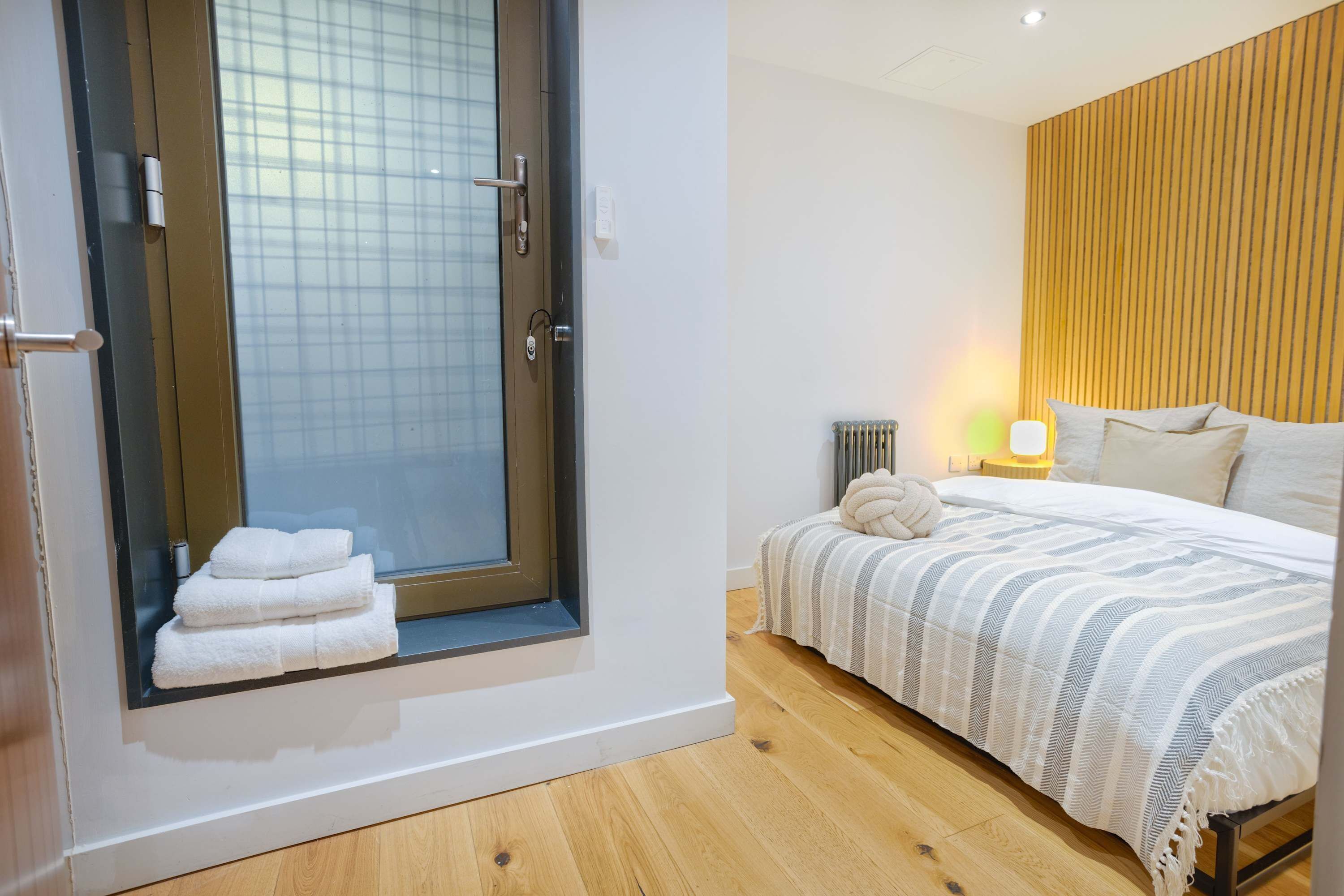 Een slaapkamer met een groot raam, een bed met een gestreept deken en een bedlamp.