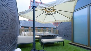 En udendørs terrasse med kunstgræs, et bord, en sofa og en stor parasol.