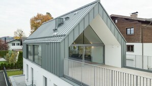 Une maison moderne à deux étages, dotée d’un balcon, de grandes fenêtres et d’un toit en pente.