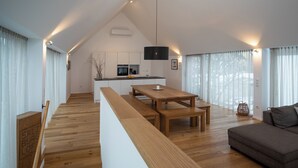 Un espace de vie moderne de style loft, avec un plancher en bois, un coin repas comprenant une table et des bancs en bois, un canapé gris et une cuisine à l’arrière-plan.