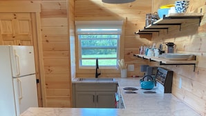A kitchen with a marble countertop, wooden cabinets, and a window with a view of greenery.