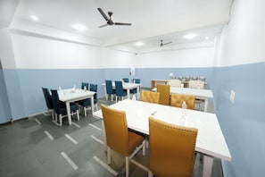 A conference room with white tables, blue chairs, and a ceiling fan. - Airport Travel Inn Deluxe  (New Delhi)