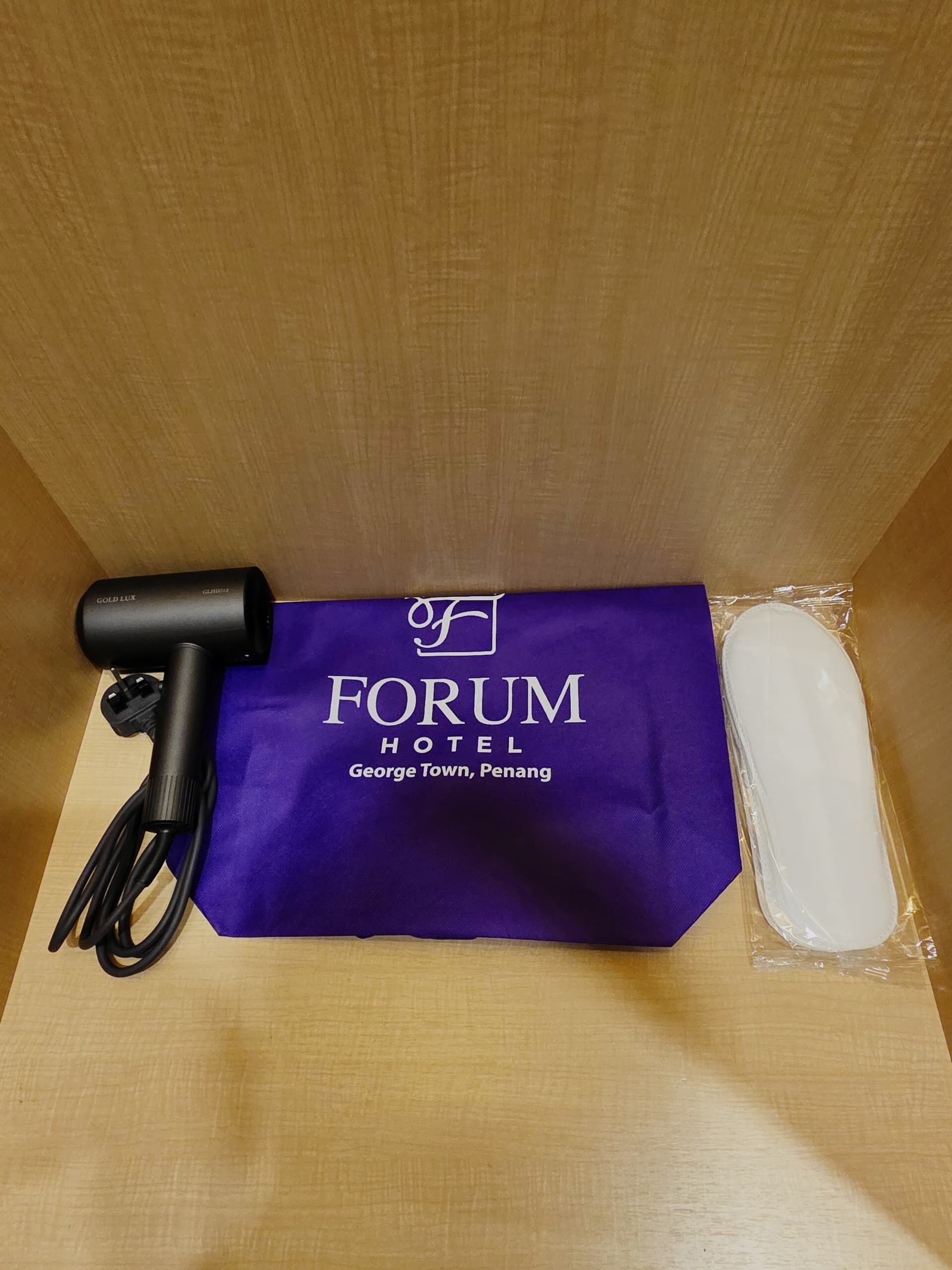 A black hairdryer, a purple hotel towel, and a white object wrapped in plastic on a wooden surface.