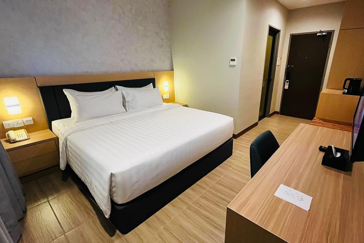 A hotel room with a large bed, bedside tables with lamps, a desk with a chair, and a television.