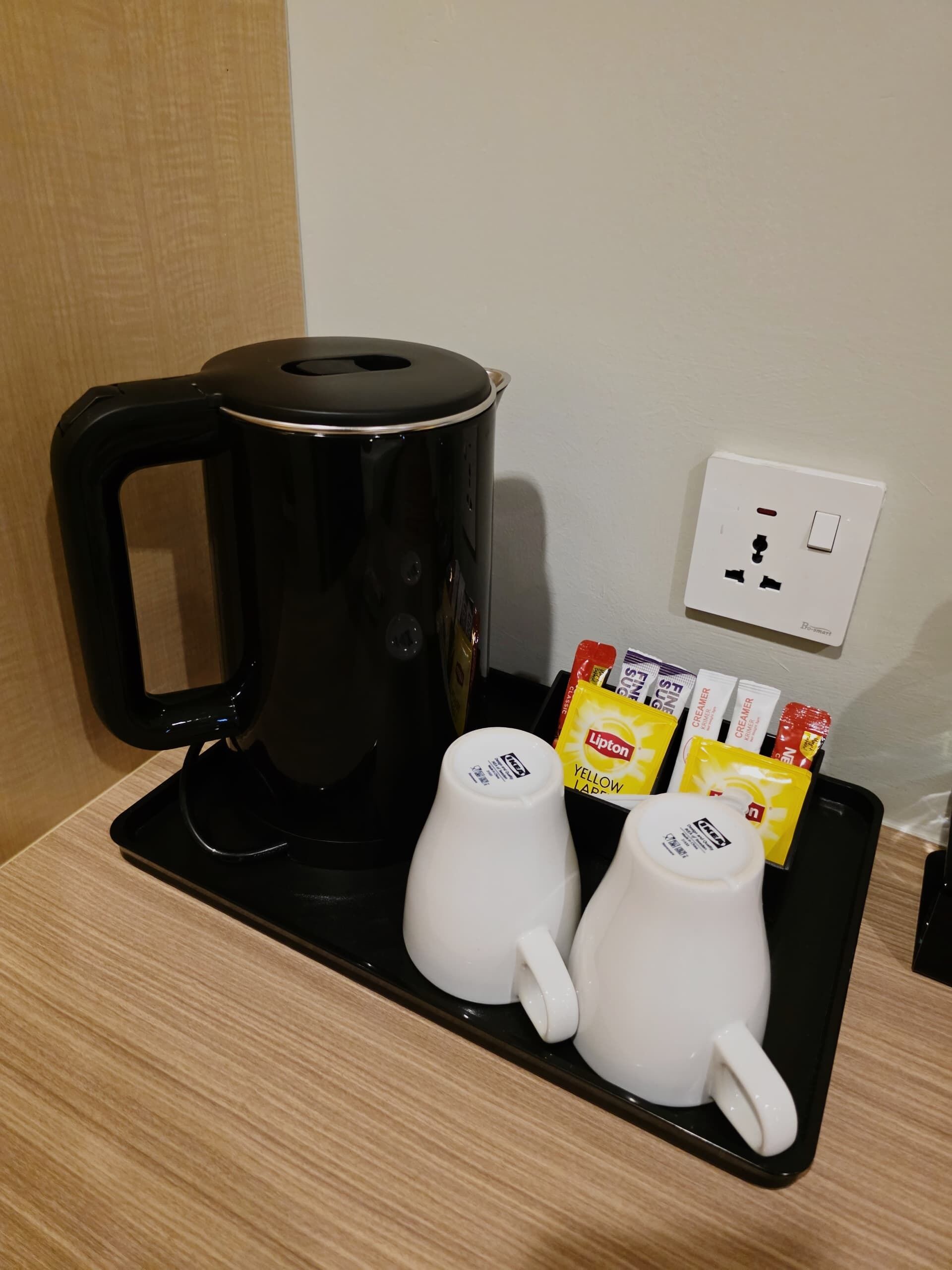 A black coffee maker on a tray with two white mugs and Lipton tea bags.
