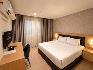 A hotel room with a bed, bedside table, nightstand, desk, chair, and a wall-mounted air conditioning unit. - Forum Hotel Penang (George Town)