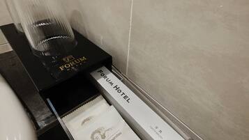 A hotel bathroom with a black tray holding a glass of water and a white paper towel dispenser labeled "Forum Hotel".