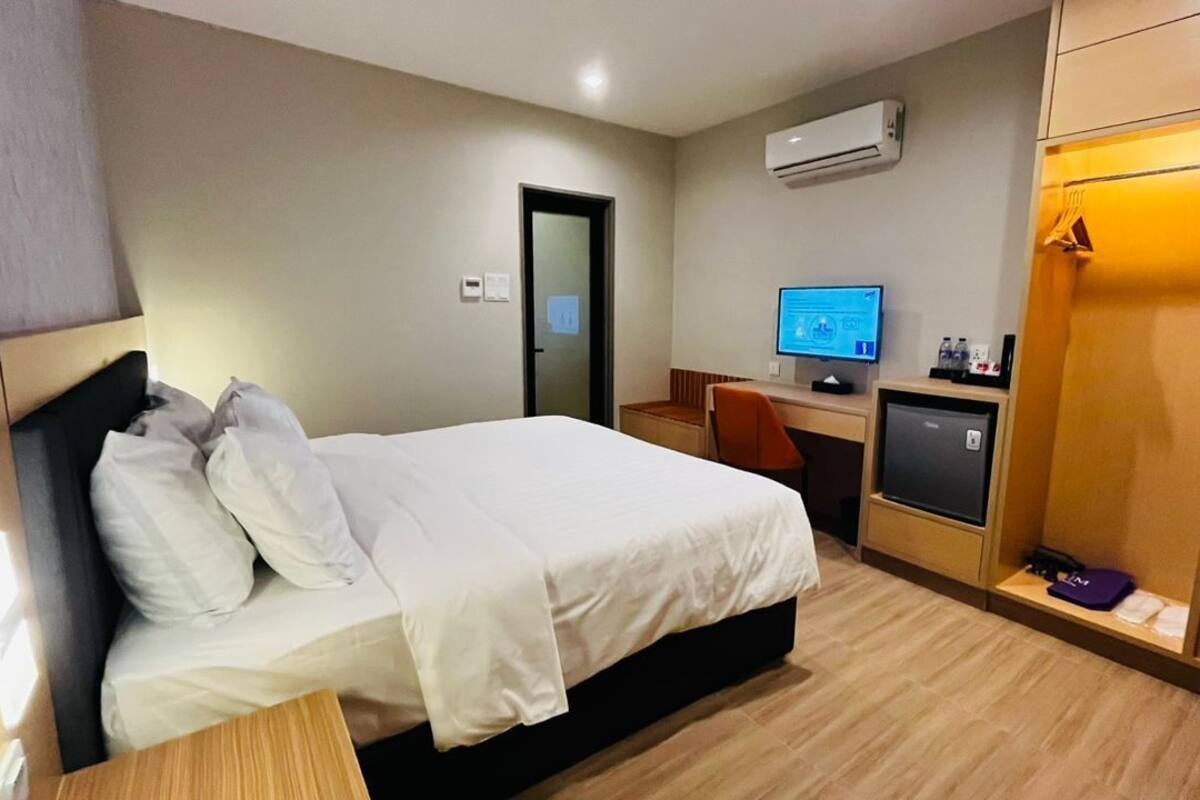 A hotel room with a bed, a desk, a computer, and a wardrobe.