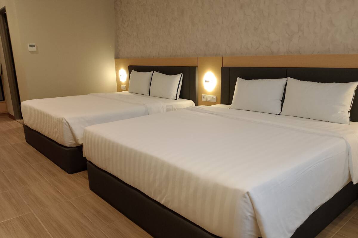 A hotel room with two single beds and a double bed, all with white linens.