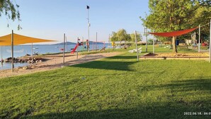 A park with a grassy area, a playground, and a body of water. - Anna Villa Apartment Badacsony (Badacsonytomaj)