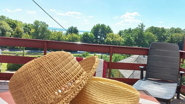 A balcony with wicker chairs and a black chair, overlooking a green landscape with trees and a distant view of a body of water. - Anna Villa Apartment Badacsony (Badacsonytomaj)