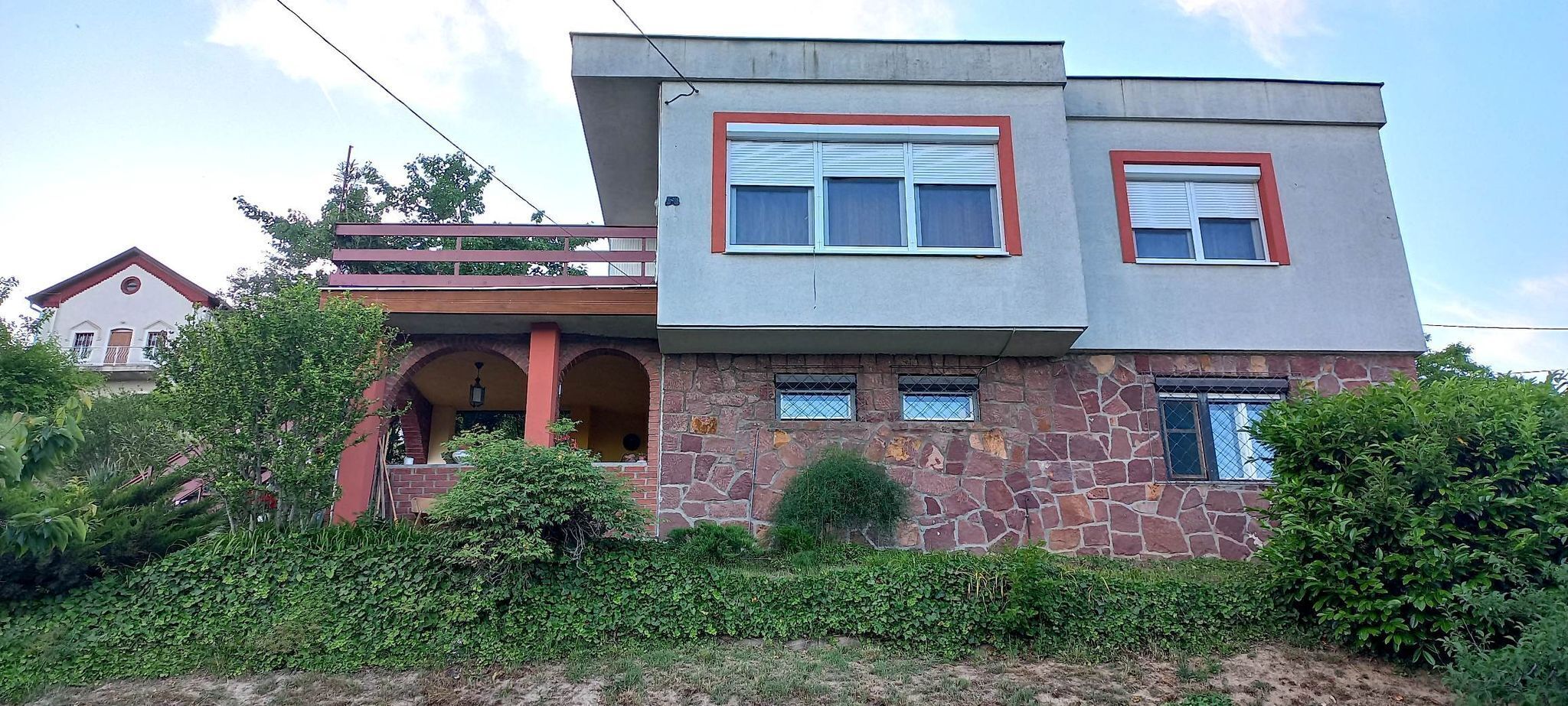 Une maison à deux étages avec une façade en pierre, un balcon et un petit porche.