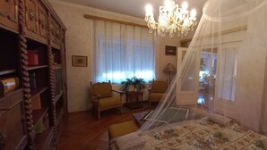 A room with a bed, a chandelier, a wooden cabinet, a chair, and a table with a plant. - Anna Villa Apartment Badacsony (Badacsonytomaj)