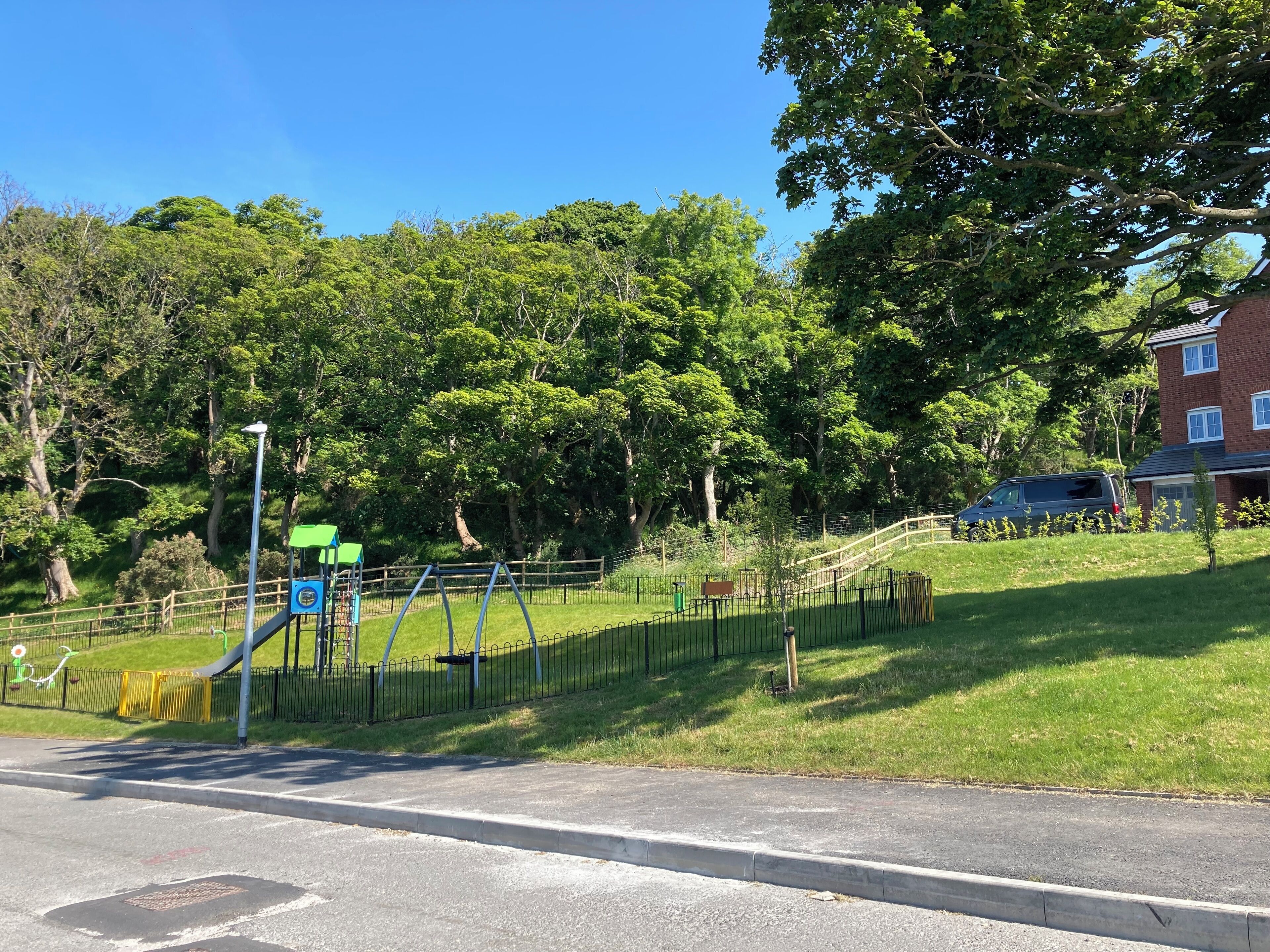 A park with a playground, a fence, and a building in the background.