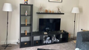 Ein Wohnzimmer mit einem Fernseher auf einer schwarzen Unterhaltungseinheit, einer Statue obenauf und einem gerahmten Bild darüber.