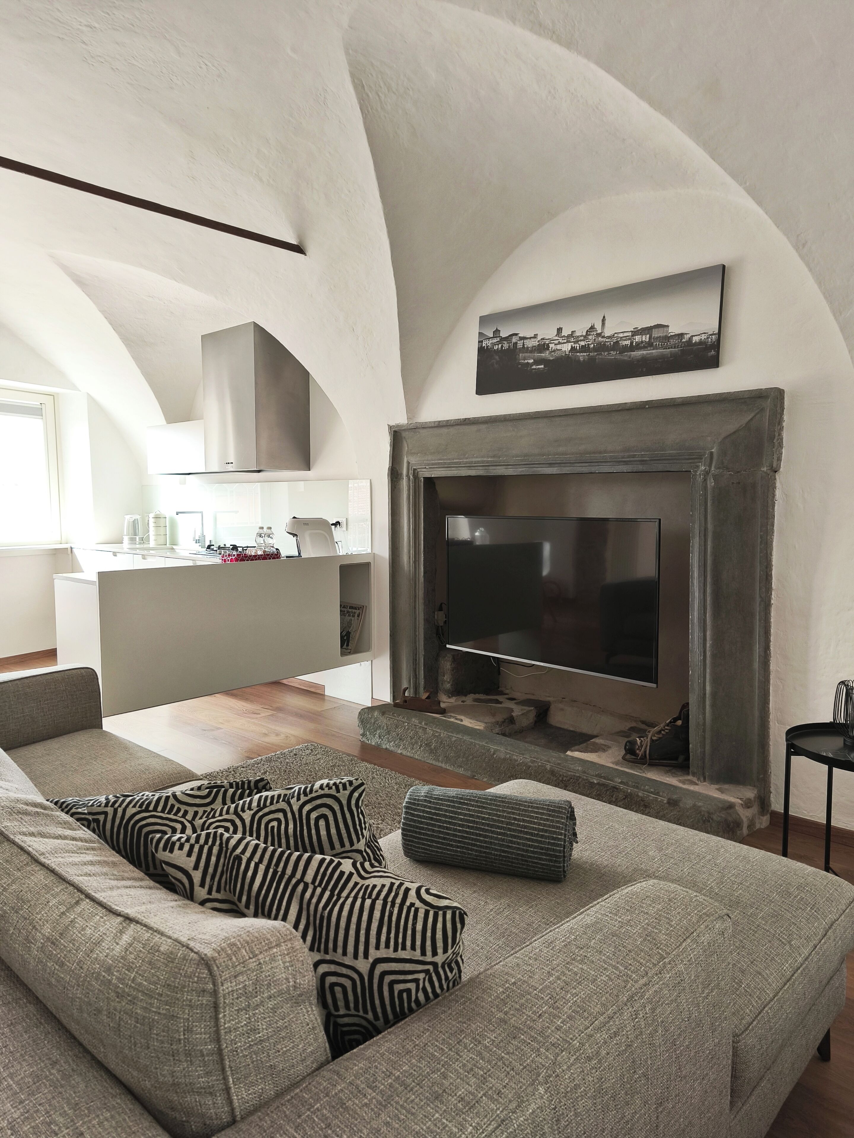 Een moderne woonkamer met een open haard, een bank met opvallende kussens, en een keuken op de achtergrond.