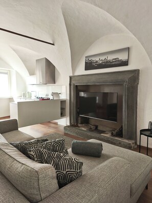 A modern living room with a fireplace, a sofa with patterned cushions, and a kitchen area in the background.