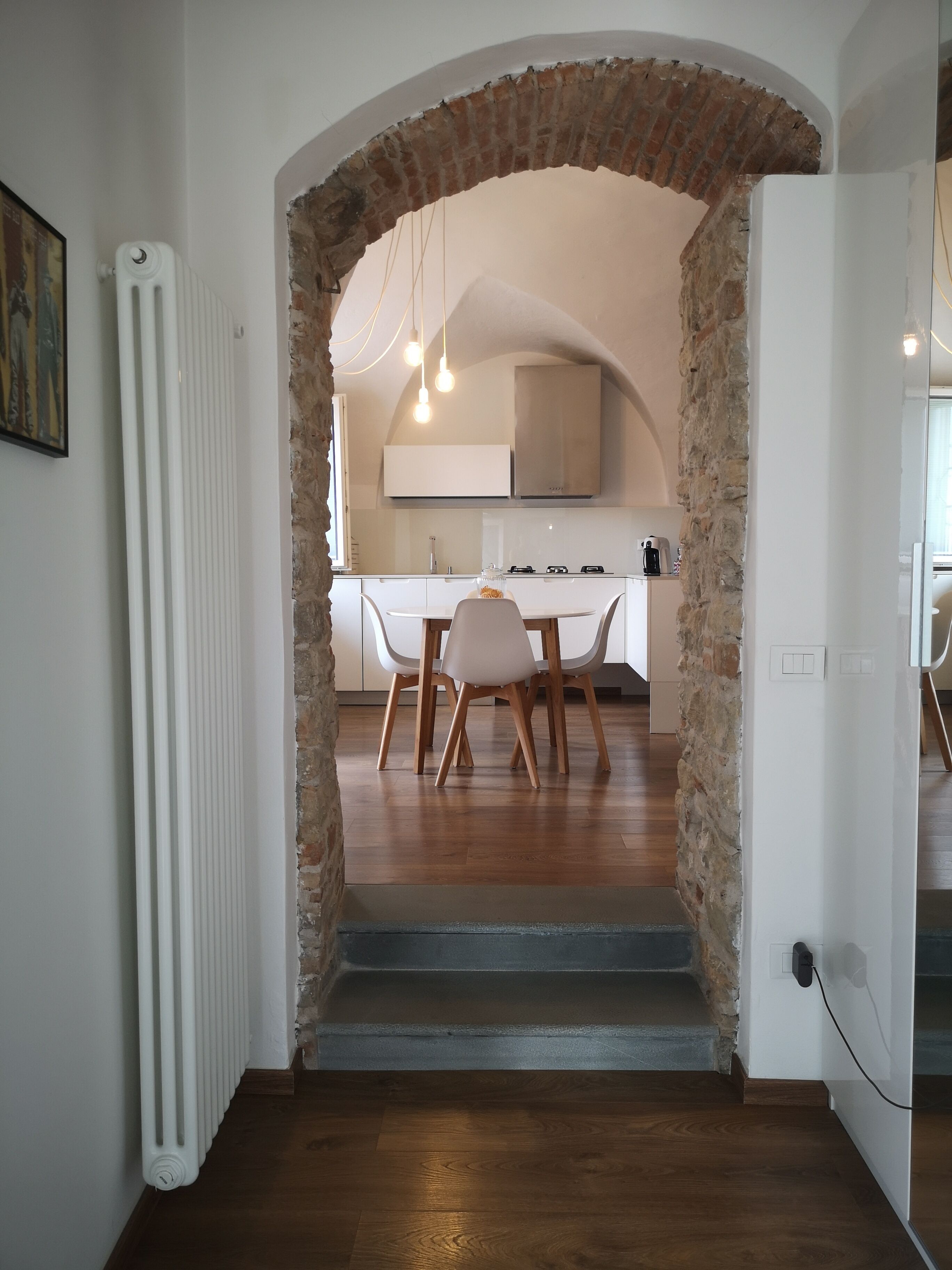 A modern kitchen with white cabinets, a brick archway, and a dining area with a wooden table and chairs.