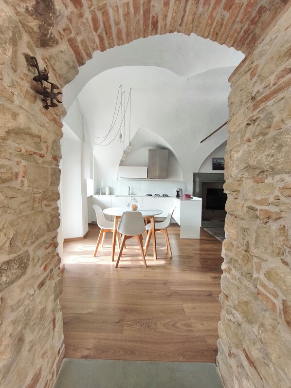 An interior with a stone archway leading to a dining area with a round table and chairs, a kitchen with white cabinets, and a hanging light fixture. - "The Pitch": A Piece of History. (Chiuduno)