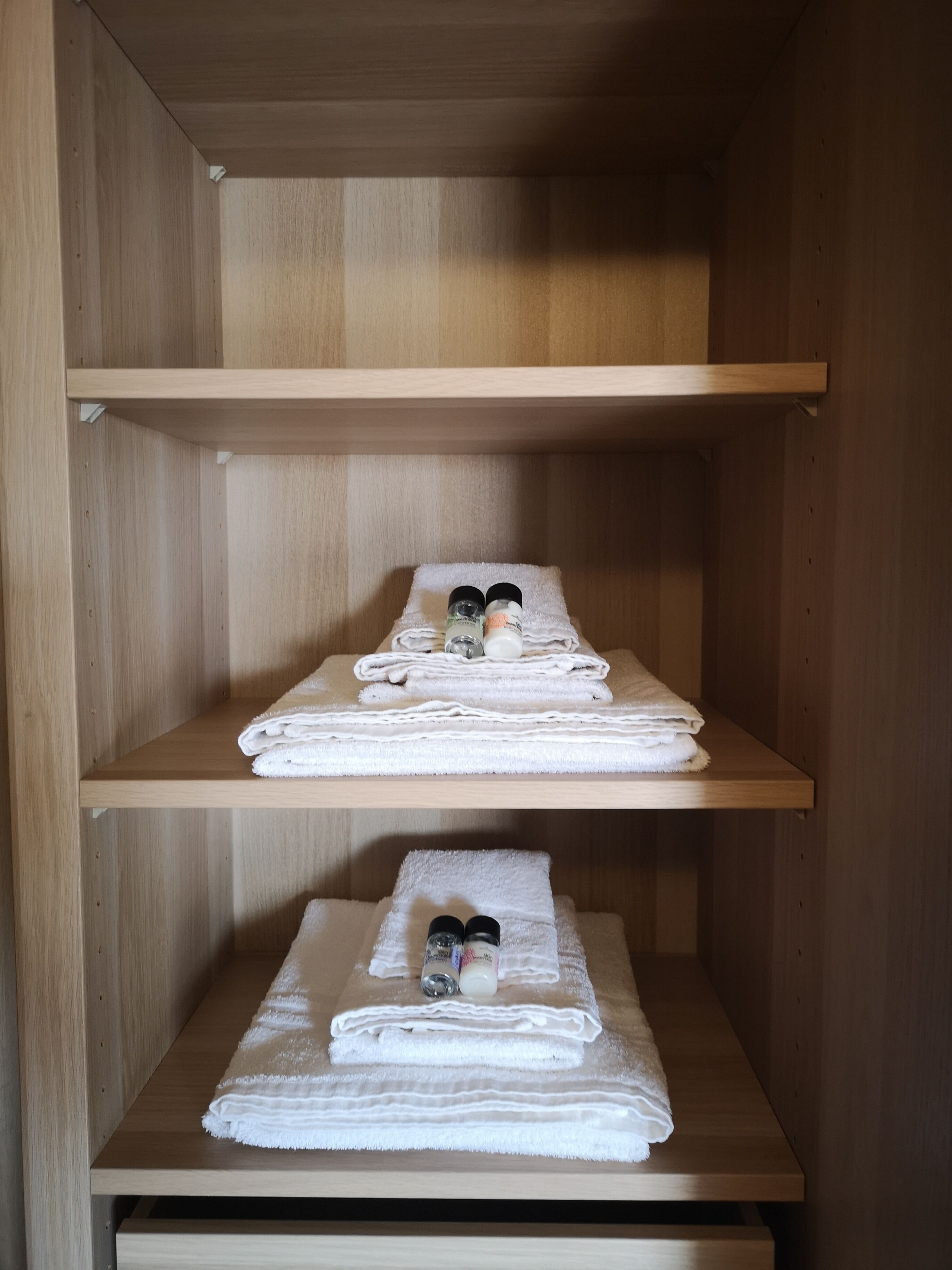 Un placard en bois avec deux étagères, chacune contenant des serviettes blanches pliées et une bouteille de lotion.