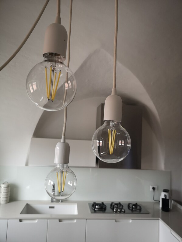 A kitchen with a white countertop, a gas stove, and three pendant lights with clear glass shades and exposed filament bulbs.