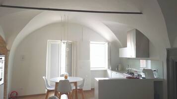 A modern kitchen with white cabinets, a dining area with a round table and chairs, and a high arched ceiling.
