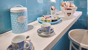 A breakfast buffet setup with a coffee container, cups, and pastries on a counter against blue tiled walls. - Magic and Enchantment, comfortable apartment in the heart of Trani's historic center (Trani)