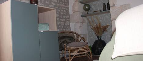 A room with a wooden wardrobe, wicker chair, and shelves with decorative items.