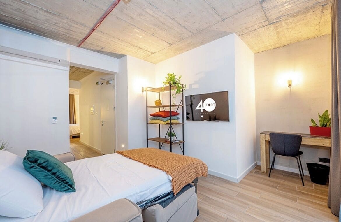 A modern bedroom with a bed, a desk, and a shelving unit with plants.