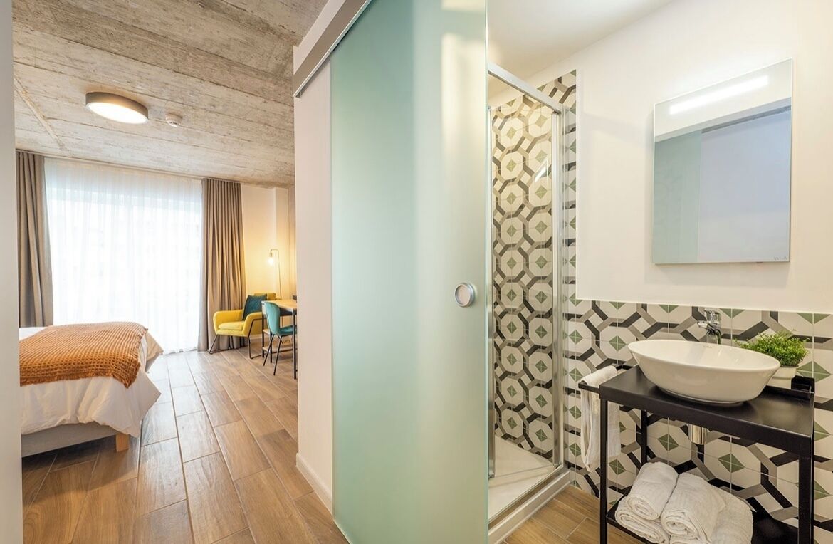 A hotel room with a bed, a desk, a chair, and a shower area.